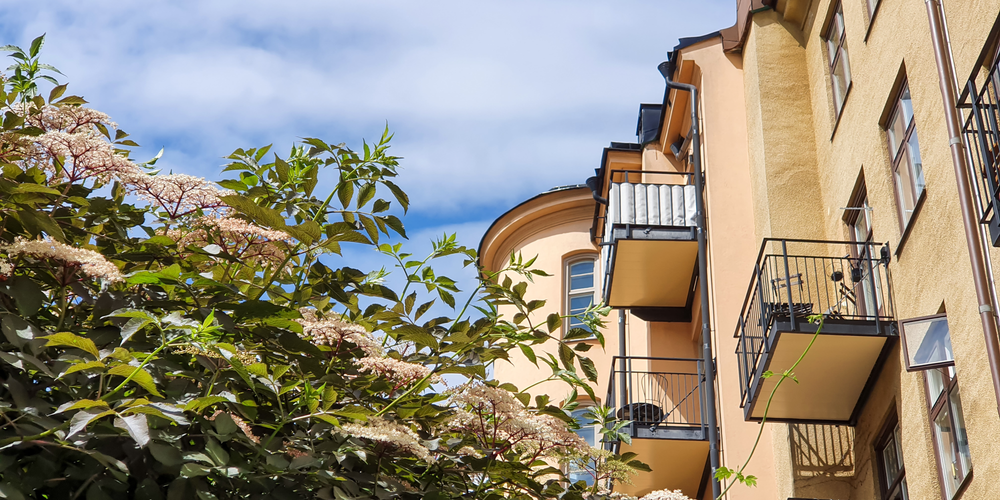 Gula bostadshus med balkonger i solsken, typisk svensk bostadsrättsmiljö.