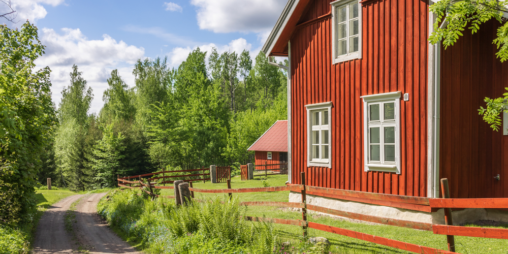 Rött hus med vita knutar vid en liten skogsväg.