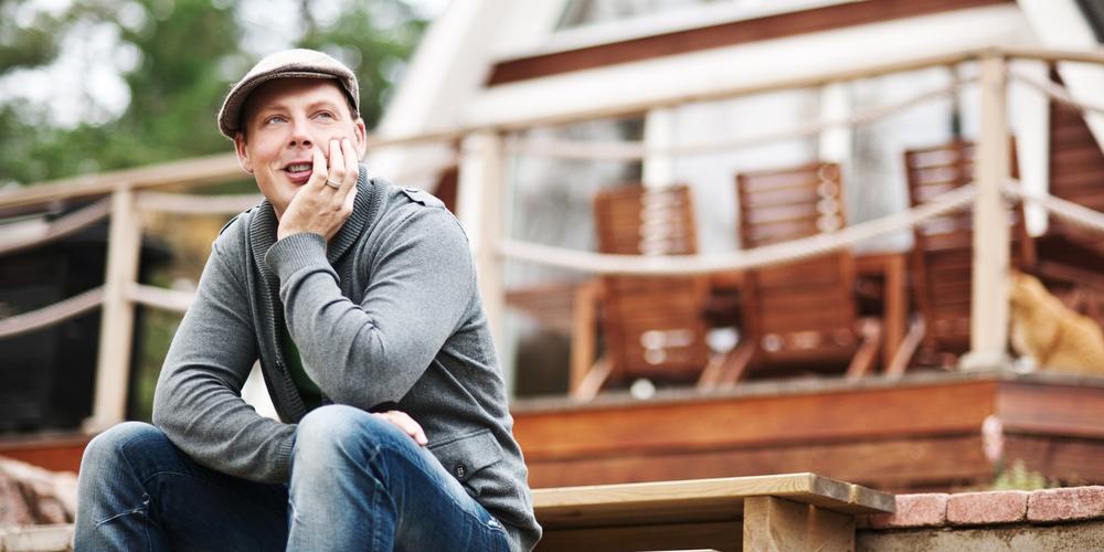 En man vid sitt hus funderar på vilken mäklare han ska välja.