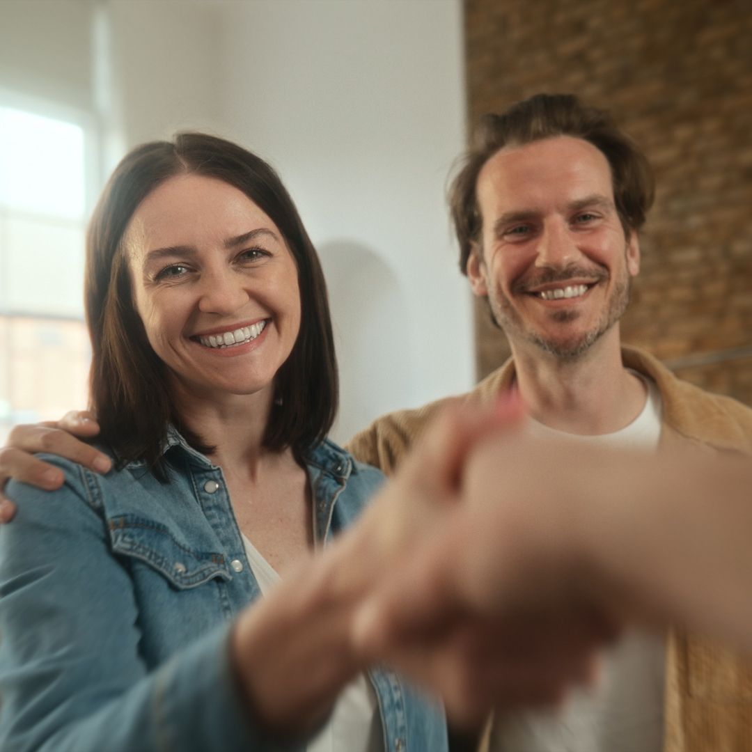Ett glatt par välkomnar en person genom att skaka dennes hand.