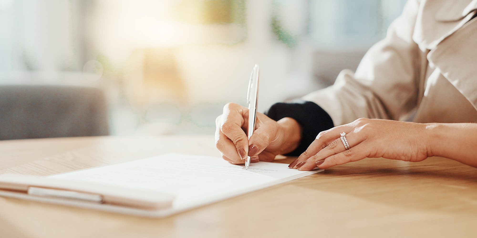 En person skriver under ett dokument med en penna vid ett bord i ett ljust rum.