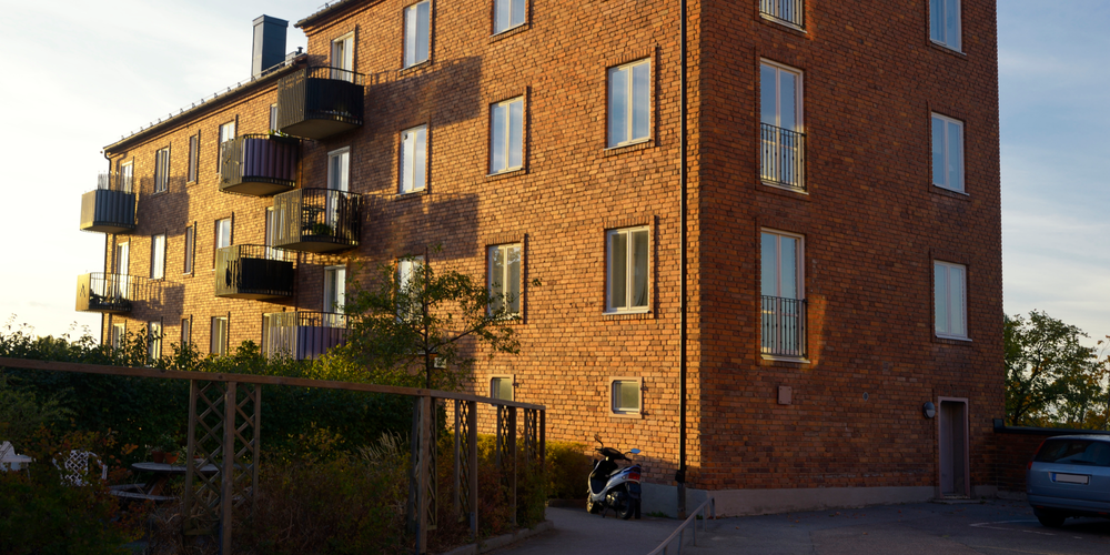 Lägenhetshus i tegel med balkonger i kvällssol.