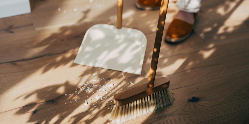 Kvinna städar med sopkvast och skyffel i solljus