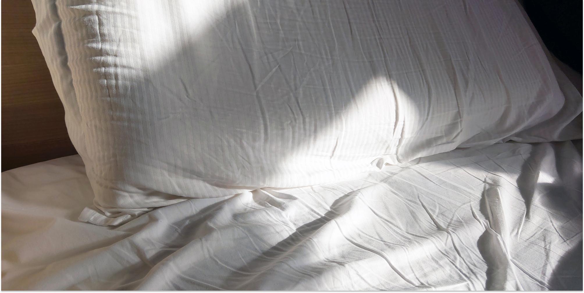 Säng med skrynkliga, vita lakan och solljus.