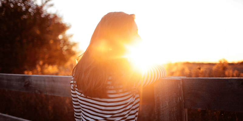 Bilde av en kvinne med ryggen til kameraet i en solnedgang