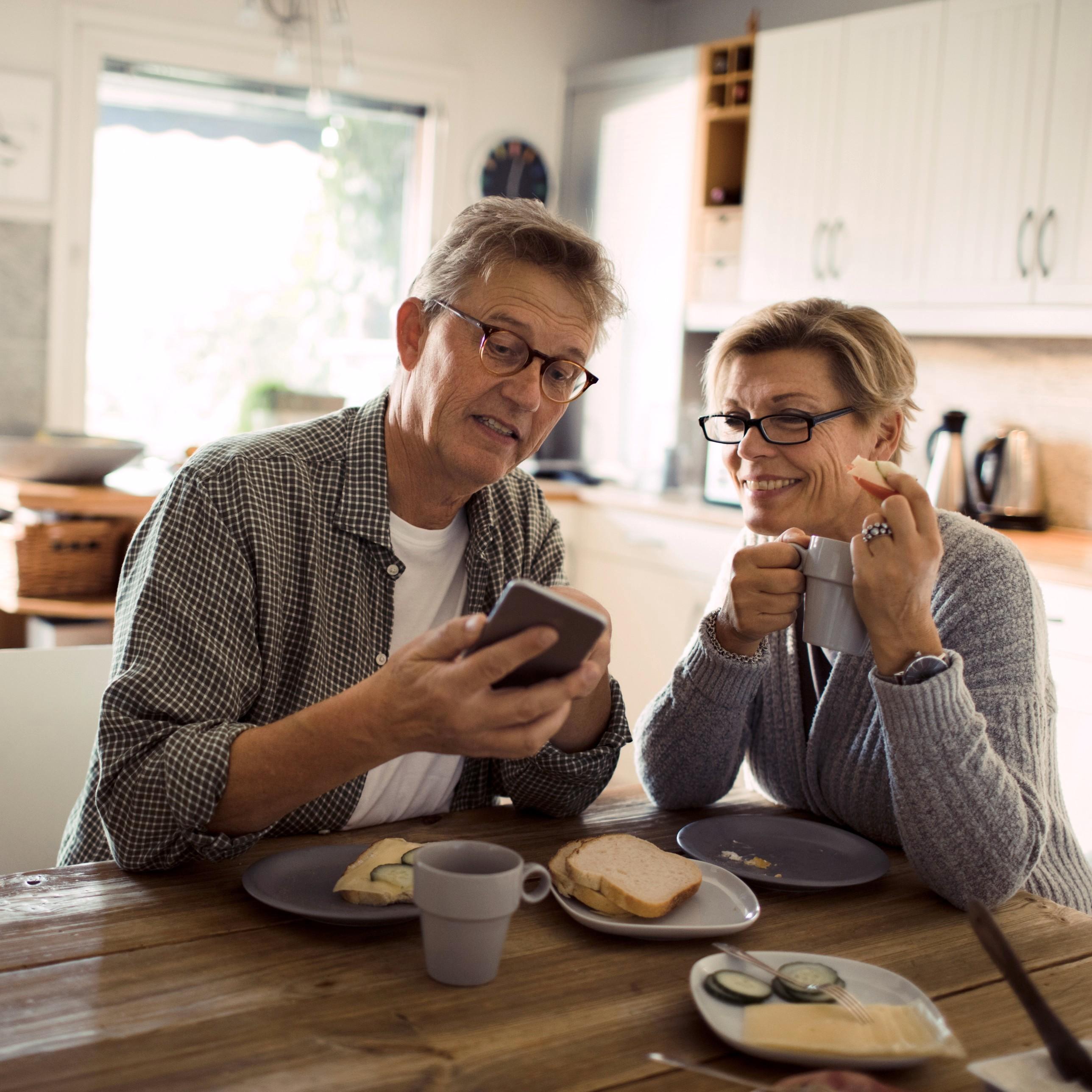 Bilde av et ektepar som spiser frokost og smiler mens de fikser seg billigere strøm på mobilen.