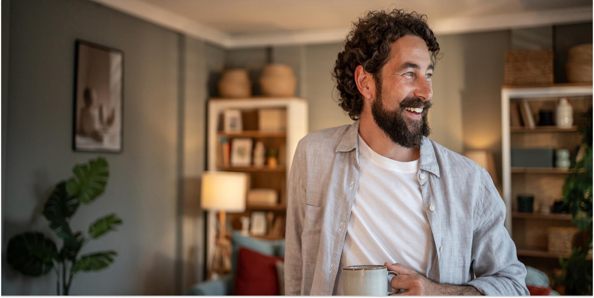 Man dricker kaffe och tittar ut genom fönstret i sitt vardagsrum