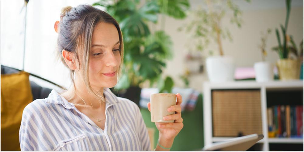 En kvinna dricker kaffe och tittar ner i sin platta. Hon funderar på vilket investeringsalternativ som blir bäst för hennes värmepump.
