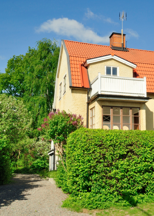 Ljusgult hus med grönskande träd runtom.
