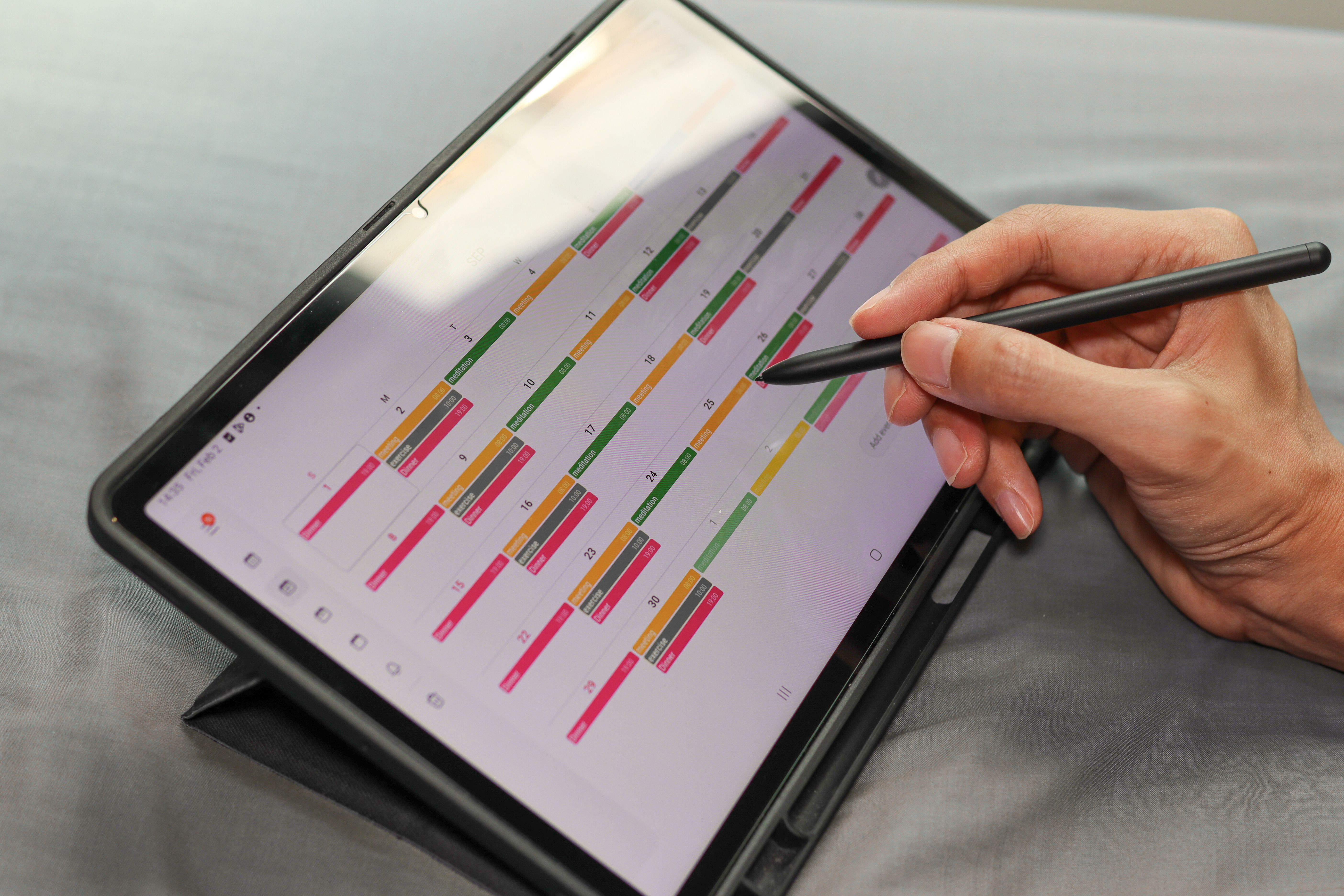 Hand mit Stift plant Termine für Kundengespräche in einem digitalen Kalender auf einem Tablet.